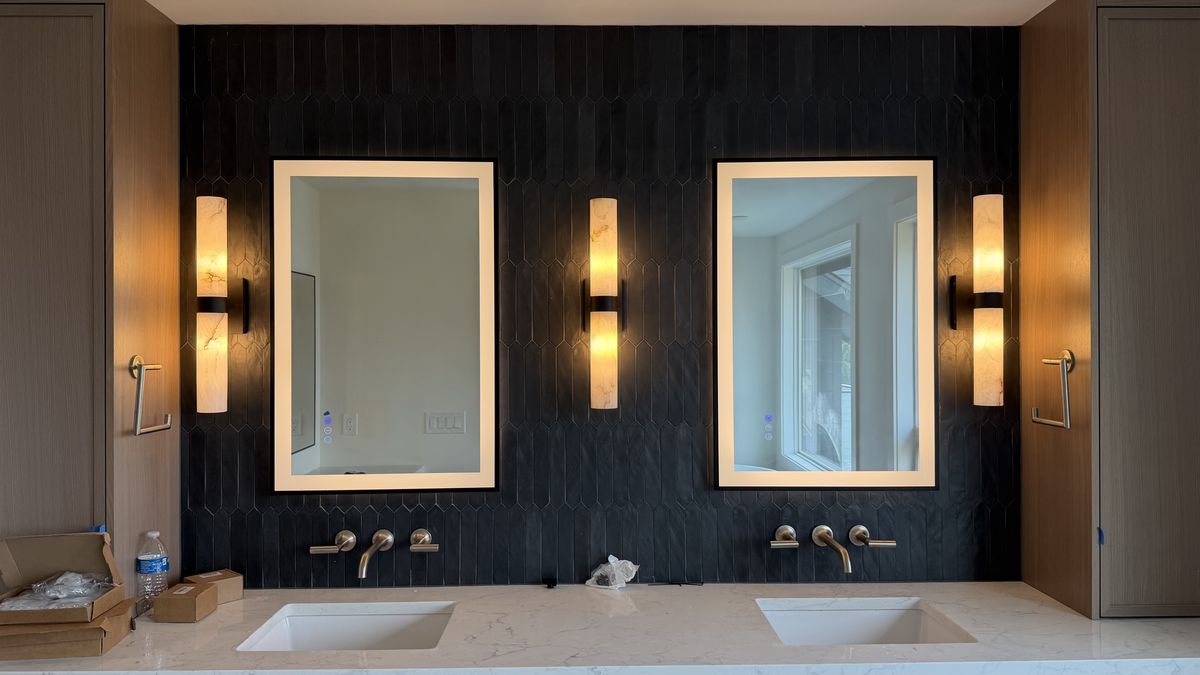 Double bathroom vanity lit by alabaster sconces and backlit mirrors