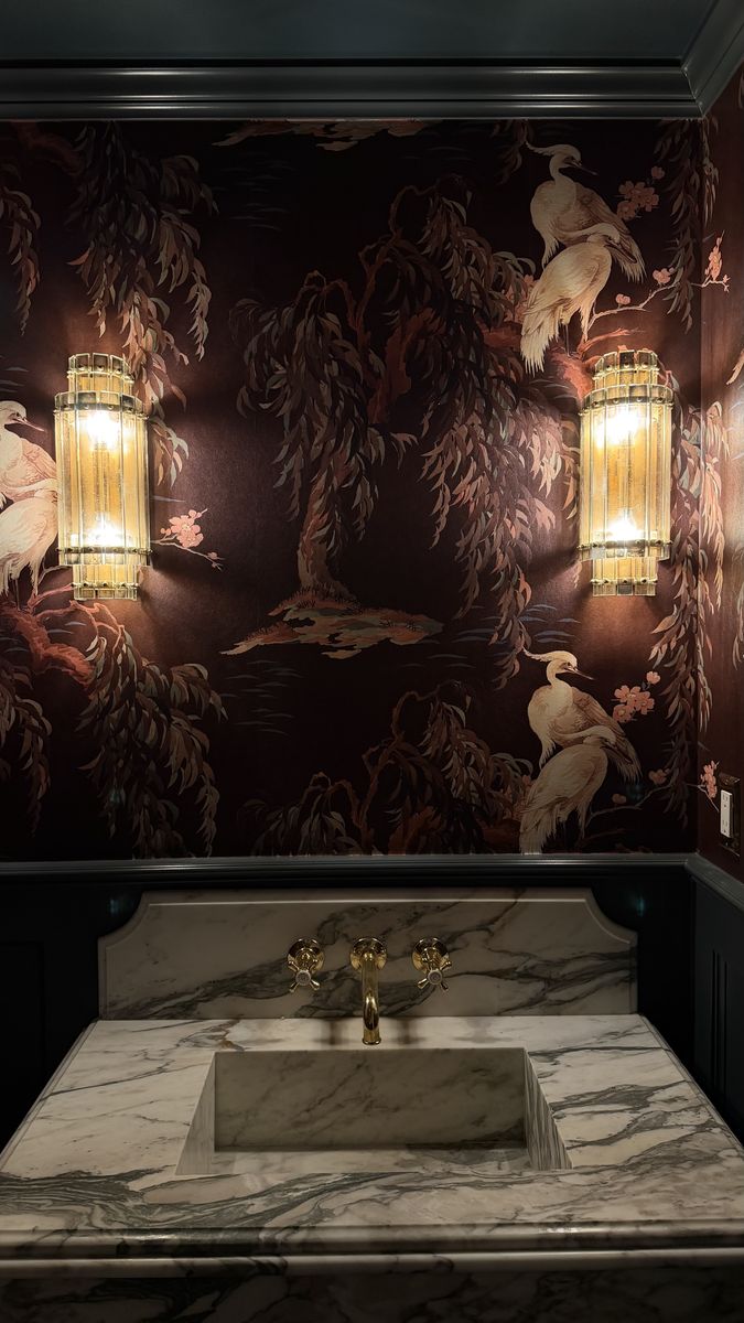Brass and glass sconces in a powder room with mural wallpaper