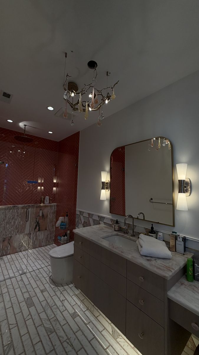 Branch chandelier, vanity sconces and recessed lights in a primary bathroom